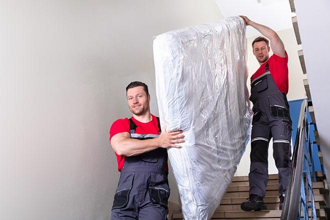 workers transporting a box spring out of a building in Steens